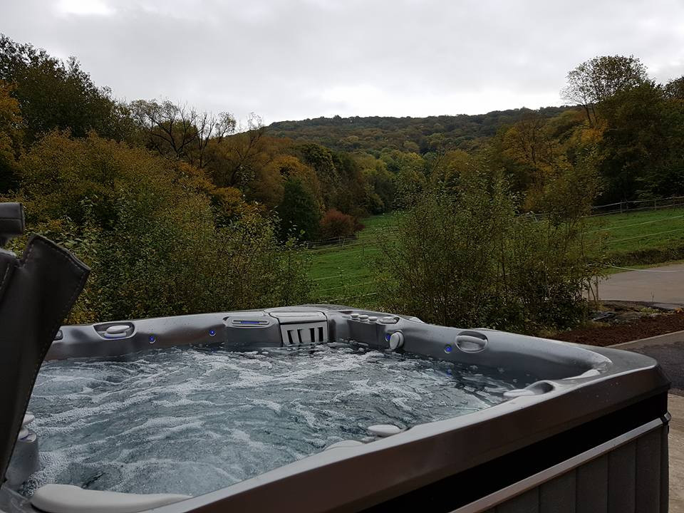 Outdoor hot tub with bubbling water overlooking a scenic countryside landscape with rolling hills and autumn foliage under an overcast sky.