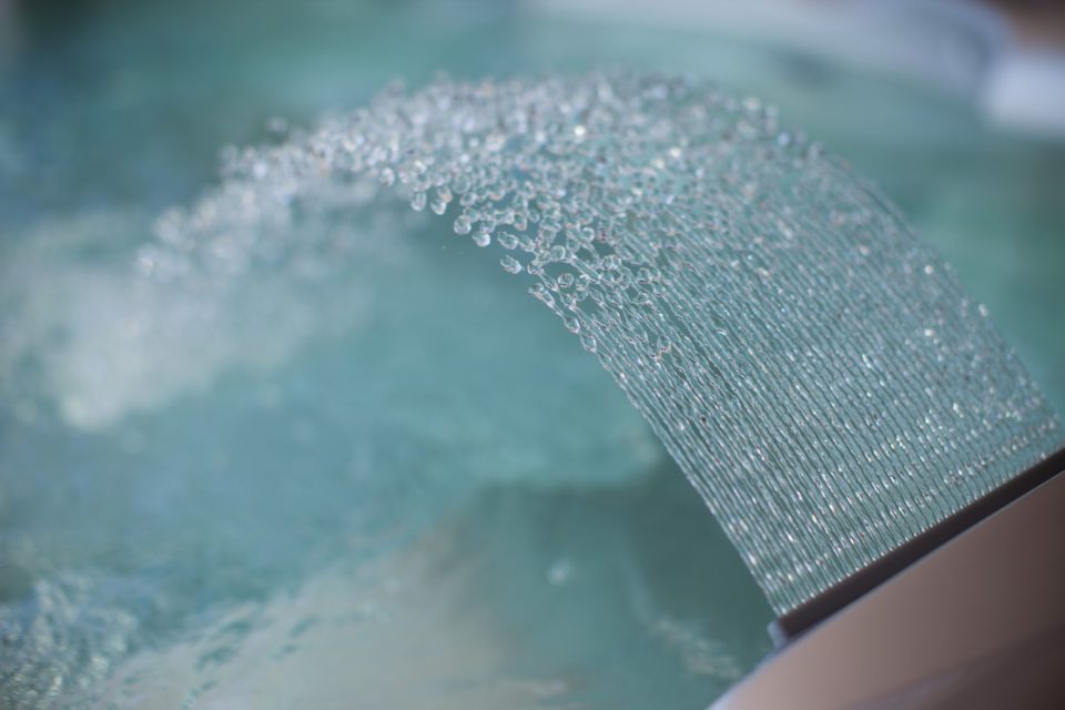 How do chlorine and other traditional sanitizers keep hot tub water clean?
