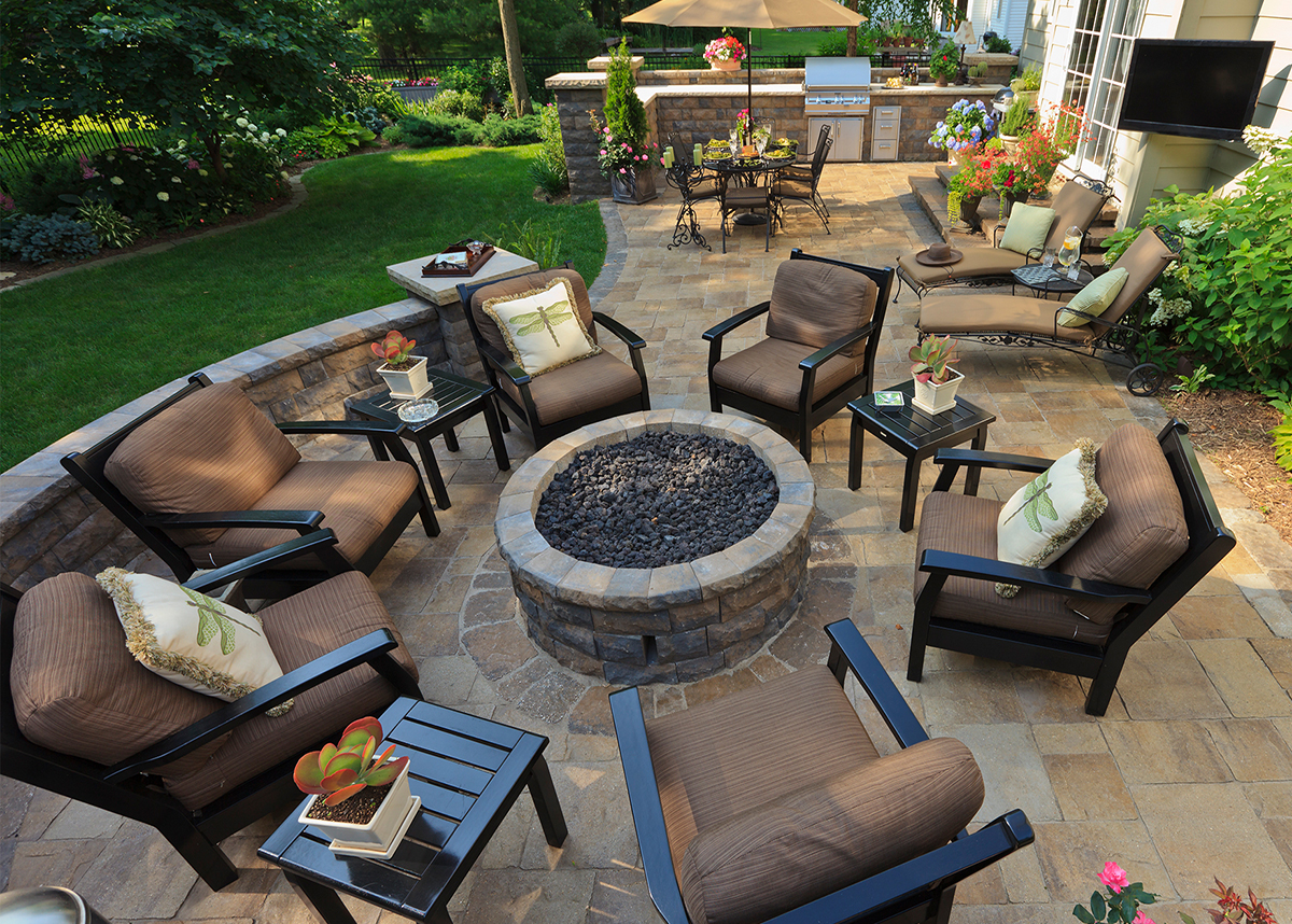 An outdoor living area with a firepit. The firepit is surrounded by comfortable seating and a lush green lawn. The image is a great example of backyard design ideas that incorporate firepits.