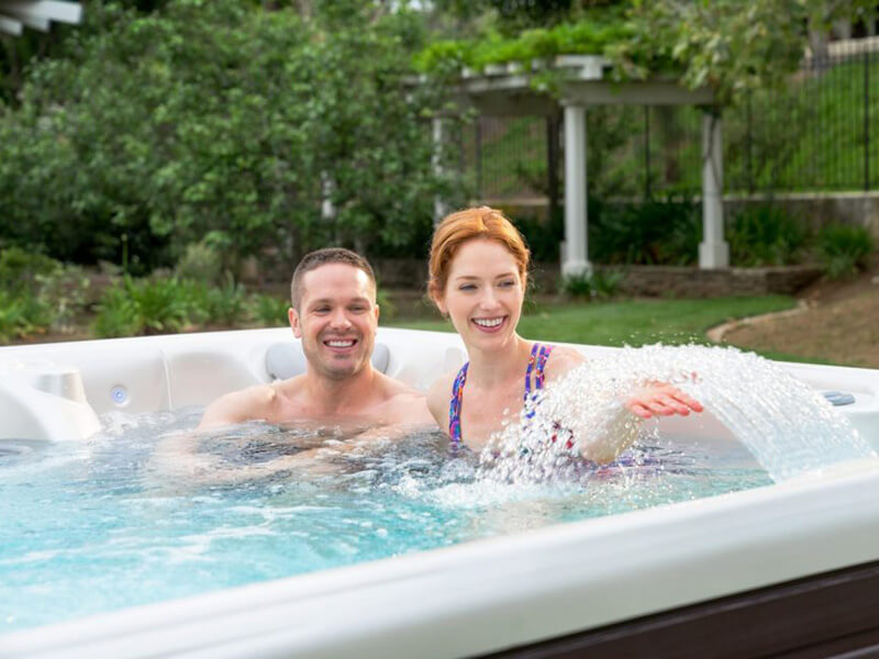 A couple enjoys the soothing fountain feature of their Caldera Spas hot tub, a testament to how luxury hot tub accessories can enhance every soak.
